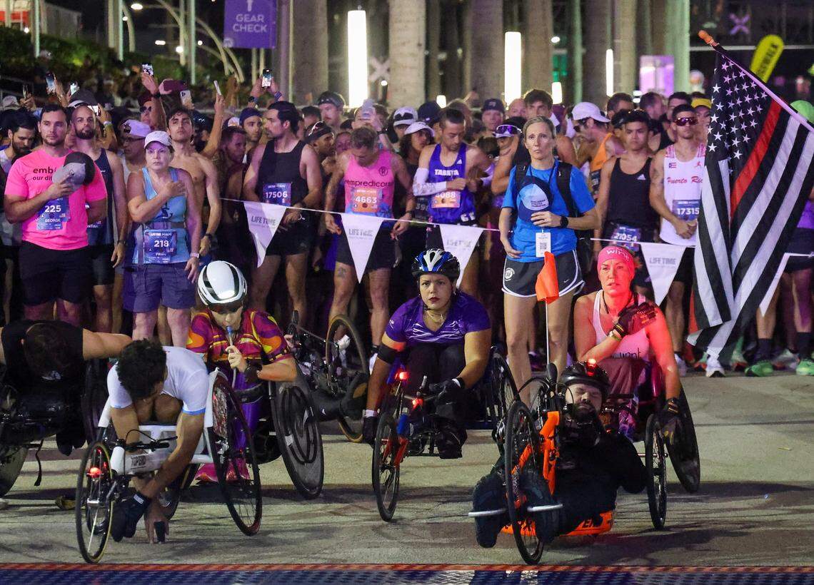 Wheelchair racers along with runners stand during the playing of the National Anthem prior to the start of the Life Time Miami Marathon at the starting line in front of the Kaseya Center on Sunday, January 28, 2024 in Miami, Florida