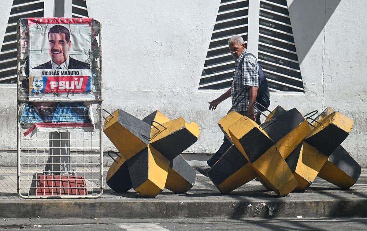 A man walks past a poster of Venezuelan President Nicolas Maduro and an anti-tank barricade in Caracas, on October 28, 2025. (Photo by JUAN BARRETO/AFP via Getty Images)          
