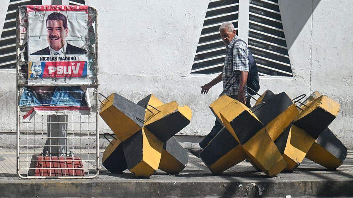 A man walks past a poster of Venezuelan President Nicolas Maduro and an anti-tank barricade in Caracas, on October 28, 2025. 