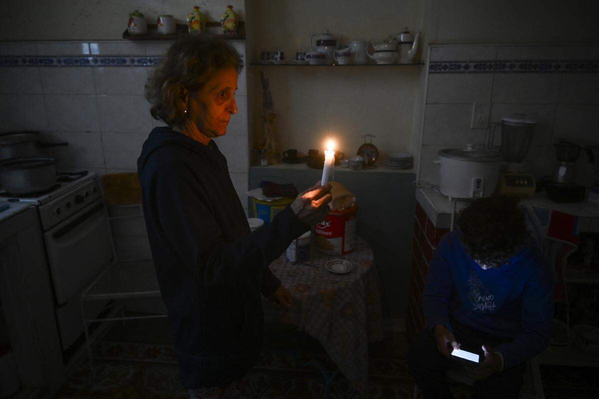 Una mujer sostiene una vela mientras un niño revisa su teléfono celular durante un apagón en el barrio de Luyano de La Habana el 28 de enero de 2026.