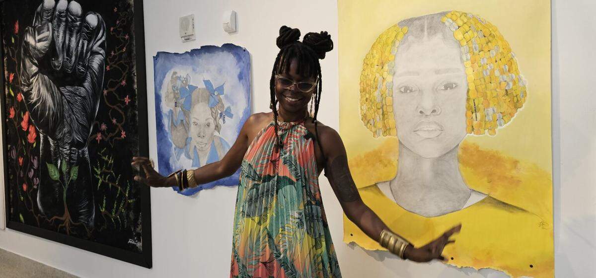 Haitian American artist Fabienne Polycarpe standing between her two artworks. Polycarpe’s art explores hair as a profound cultural symbol, reflecting both Haitian traditions and Black American influences. On her left, an artwork by Rico Melvin Costoso Jr. titled “Black Power.”