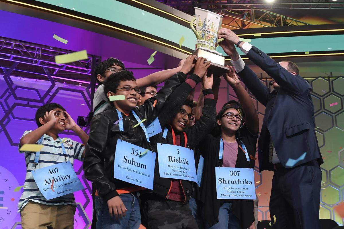 Abhijay Kodali (407), 12, of Flower Mound, Texas; Sohum Sukhatankar (354), 13, of Dallas; Rishik Gandhasri (5), 13, of San Jose, Calif.; Shruthika Padhy, 13, of Cherry Hill, N.J., and the other winning spellers gather together at the end of the 2019 Scripps National Spelling Bee in Oxon Hill, Md., early Friday, May 31, 2019. The Bee ended in an unprecedented 8-way championship tie after organizers ran out of challenging words. E.W. Scripps Company Chief Executive Officer Adam Symson, right, helps present the trophy.