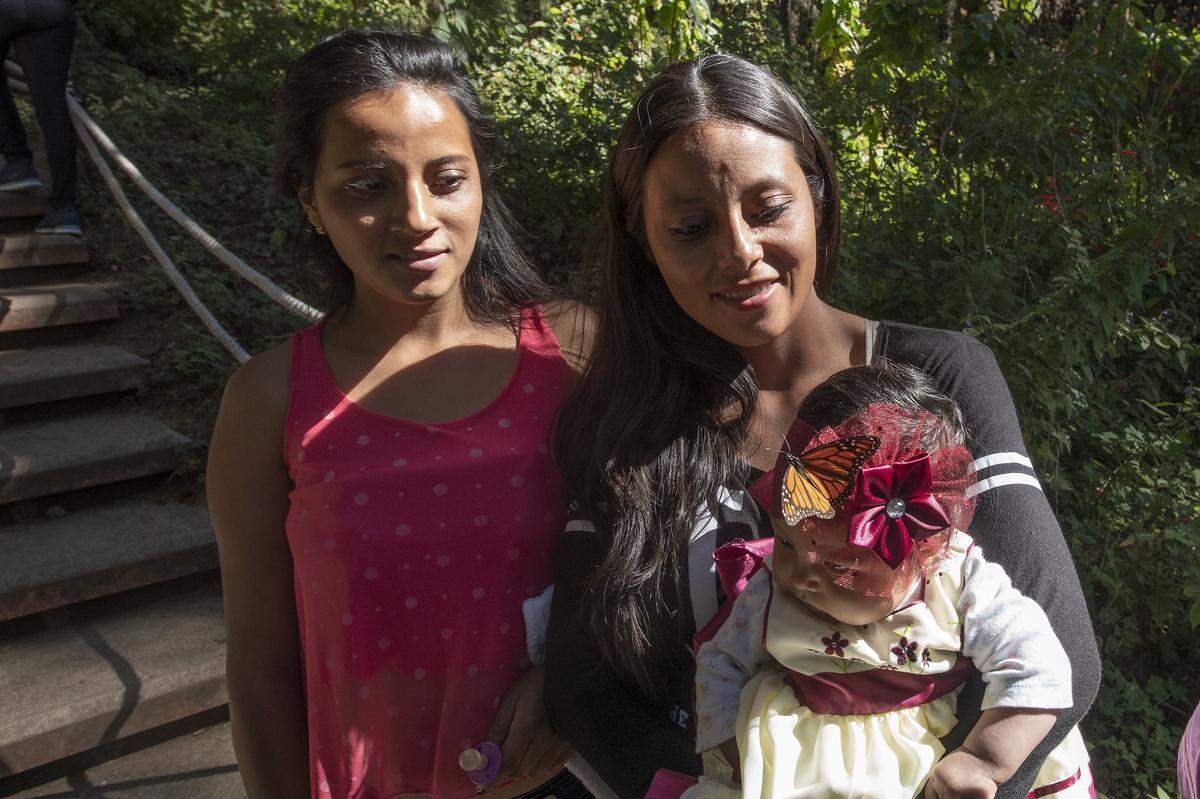A monarch lands on the head of a baby as her mother and aunt look on at El Rosario Butterfly Sanctuary.