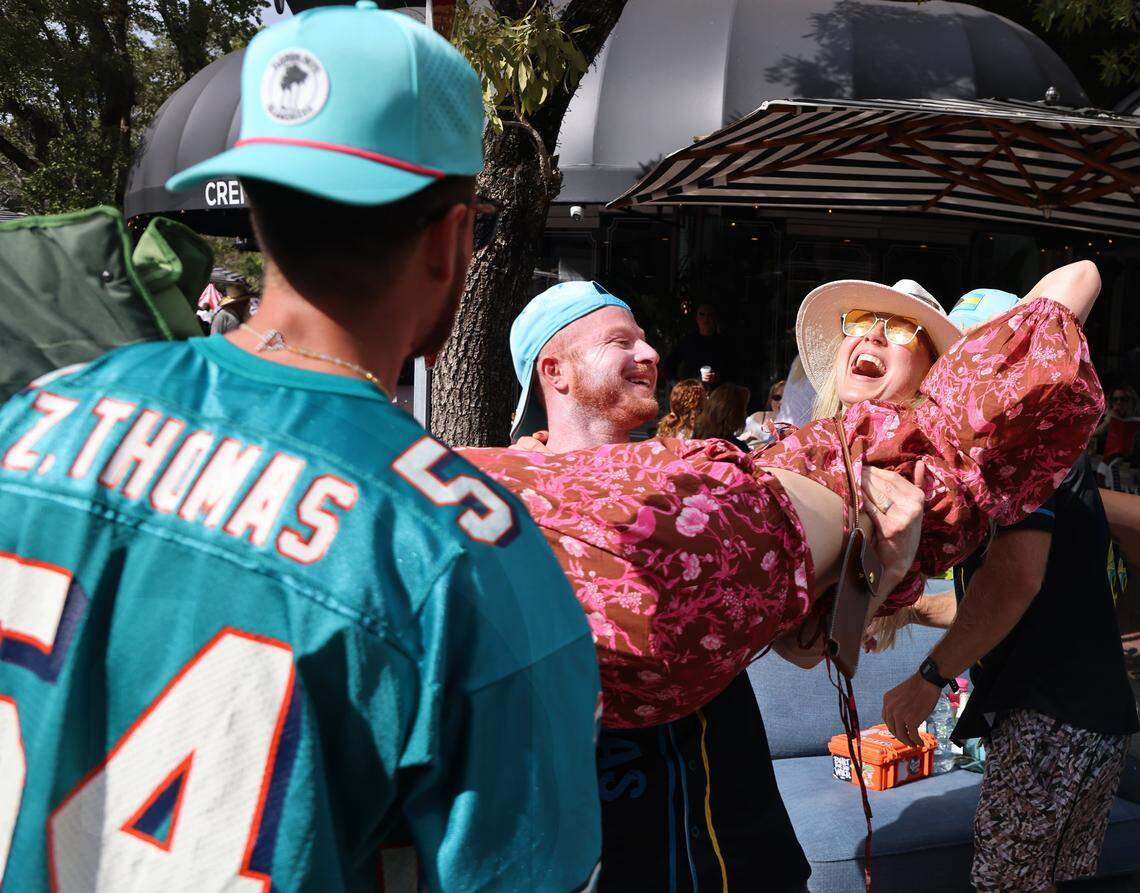 Grovites Baker Newman, center, lifts his wife Caroline Newman, right, while greeting one another as she arrives to join him at the Coconut Grove King Mango Strut parade. The 42nd Annual King Mango Strut - a wacky, fun-filled parade celebrating the quirks, humorous, and satirical political statements held on Sunday, January 4, 2026, in the heart of the Grove in Miami, Florida. 