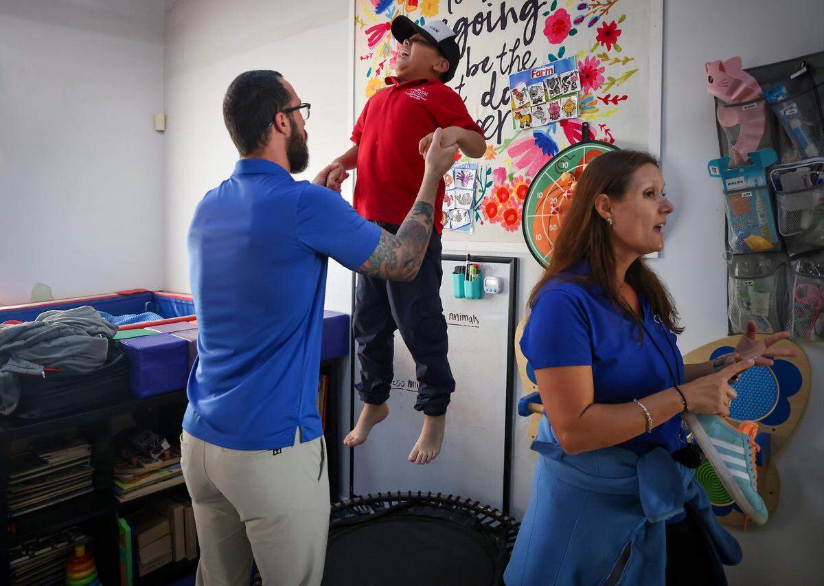 OTR David Balletti, left, holds the hands of Ethan Morejon, 7, center, while he bounces in the occupational therapy gym. The Miami Herald was given tour of the school as it tries to continue to serve the needs of children with autistic students on Monday, September 23, 2025.