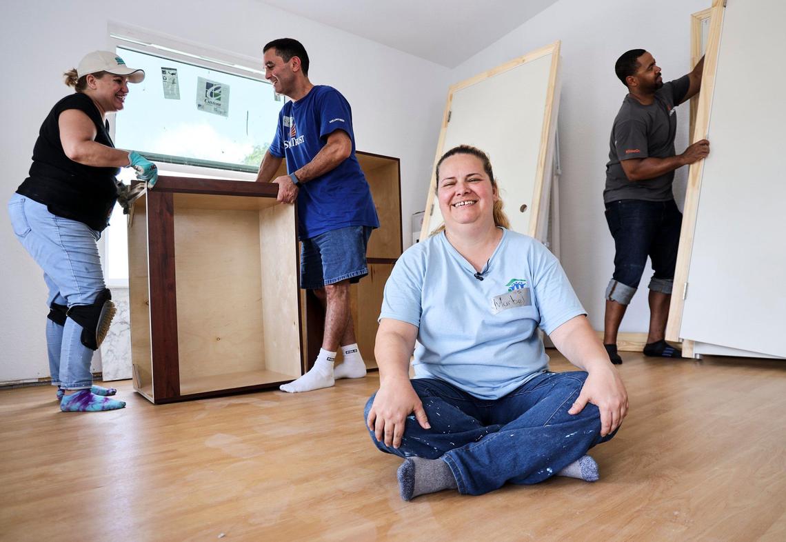 Maribel Gonzalez, 41, sits on the newly installed floor of her Habitat for Humanity of Greater Miami home in South Miami-Dade’s Goulds neighborhood, while volunteers Vivian Marazzi, left, Alex Navarro and Keir Rocha, right, bring in newly delivered doors and cabinets. Gonzalez and seven other new soon-to-be homeowners are helping hammer together their houses during Habitat’s annual Blitz Build. The nonprofit recently marked 30 years in operation.