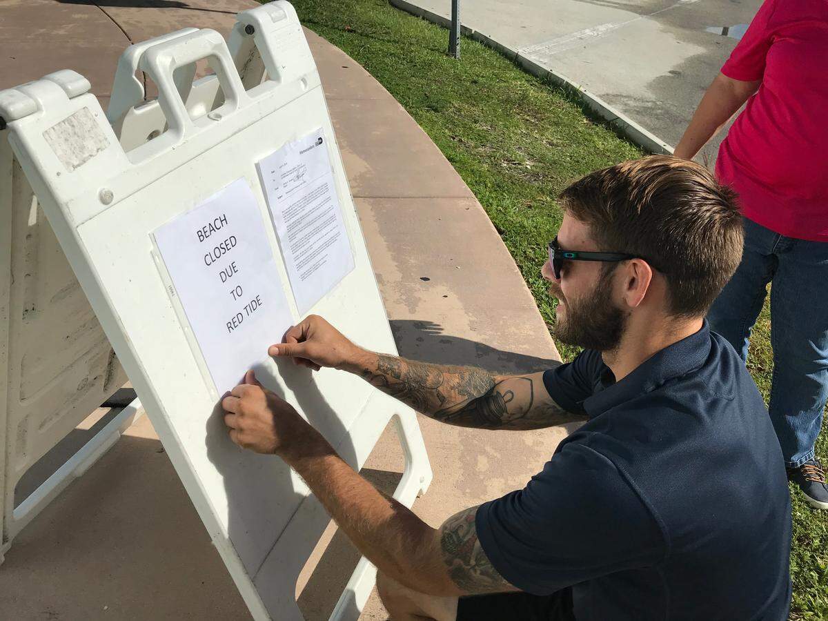 Haulover Park manager Pedro Perez readies a sign to turn away parkgoers, stating the county park has been closed due to red tide on Thursday, Oct. 4, 2018.