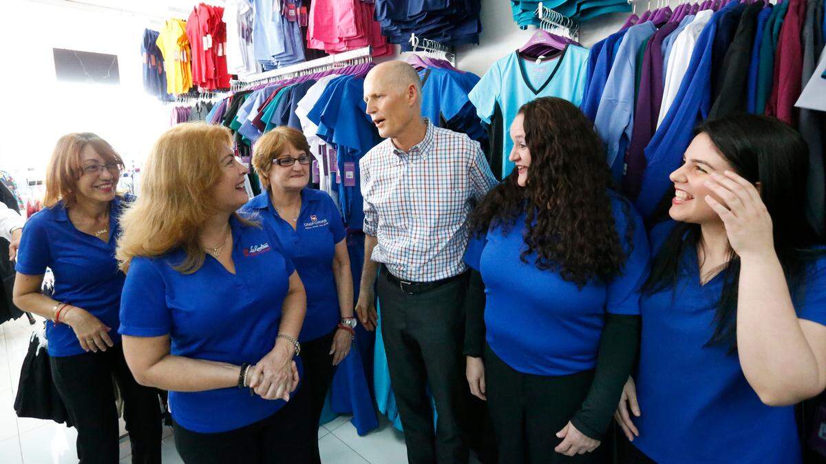 Florida Gov. Rick Scott, center, chats with employees of LR Uniforms in Miami after Scott held a news conference in their store Wednesday to highlight the Back-To-School Sales Tax Holiday. The sales tax holiday is set for Friday through Sunday, Aug. 3-5. But this year Florida lawmakers took technology items, like computers, off the tax-free eligible list.