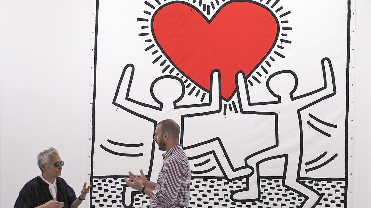 On Tuesday, Nov. 26, 2019, patron and collector Mera Rubell, left, greets Patrick Goddard, president of Brightline, right, as he tours the Rubells’ Keith Haring collection. Brightline trains and the Rubell Museum are collaborating to pair their trains with designs from the late artist. Keith Haring, Untitled, 1982, acrylic on vinyl tarpaulin, 180 x 180 in. (4570 x 4570 cm), acquired in 1982. © Keith Haring Foundation. Work courtesy of the Rubell Museum.