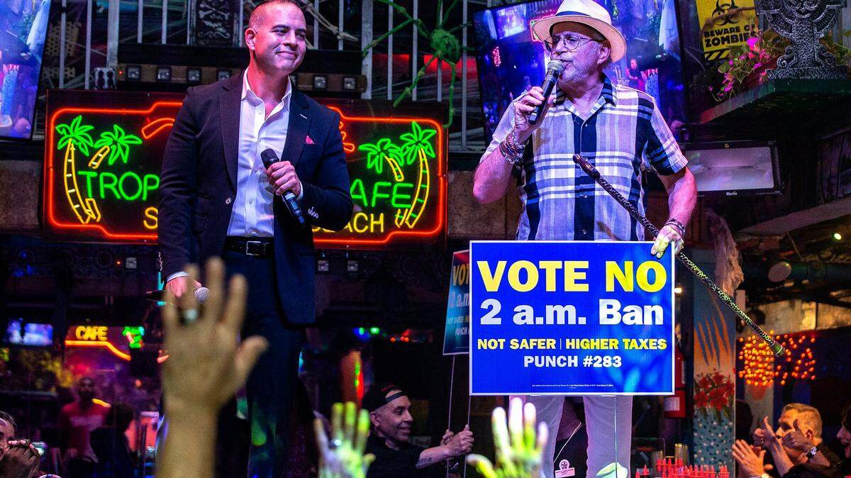 El propietario de MangoTropical Cafe, David Wallack (derecha), se dirige a la multitud con la ayuda del artista Alex Ruiz mientras personas mayores de Miami Beach disfrutan de comida y bebidas gratis en un evento de campaña política en el bar de Ocean Drive el miércoles 6 de octubre de 2021. 
