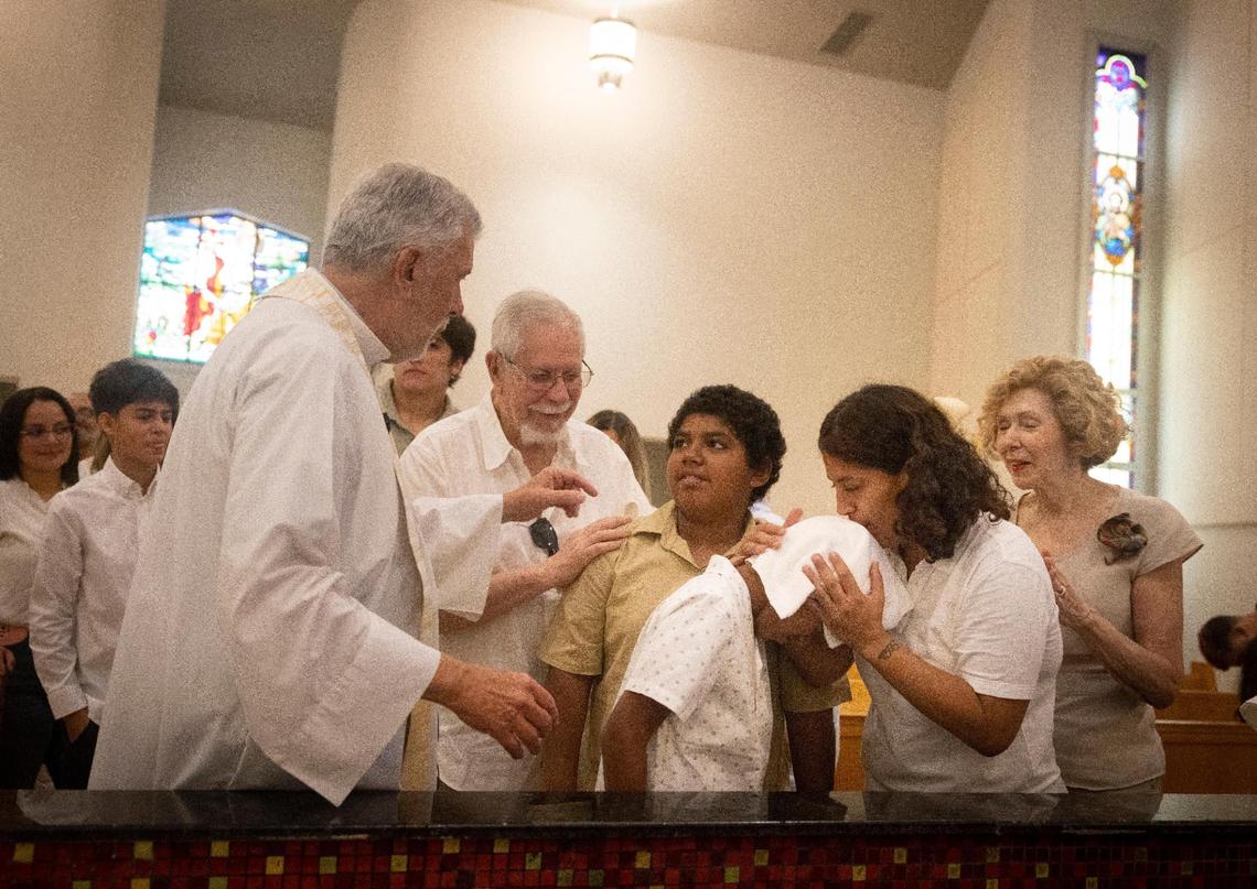 Evelyn Diaz gaviria, right, kisses her son, Jeremiah Diaz, on the head after his baptism ceremony while his brother, Josiah Perez Diaz, awaits his turn on Sunday, Sept. 10, 2023, at Corpus Christi Catholic Church in Miami.
