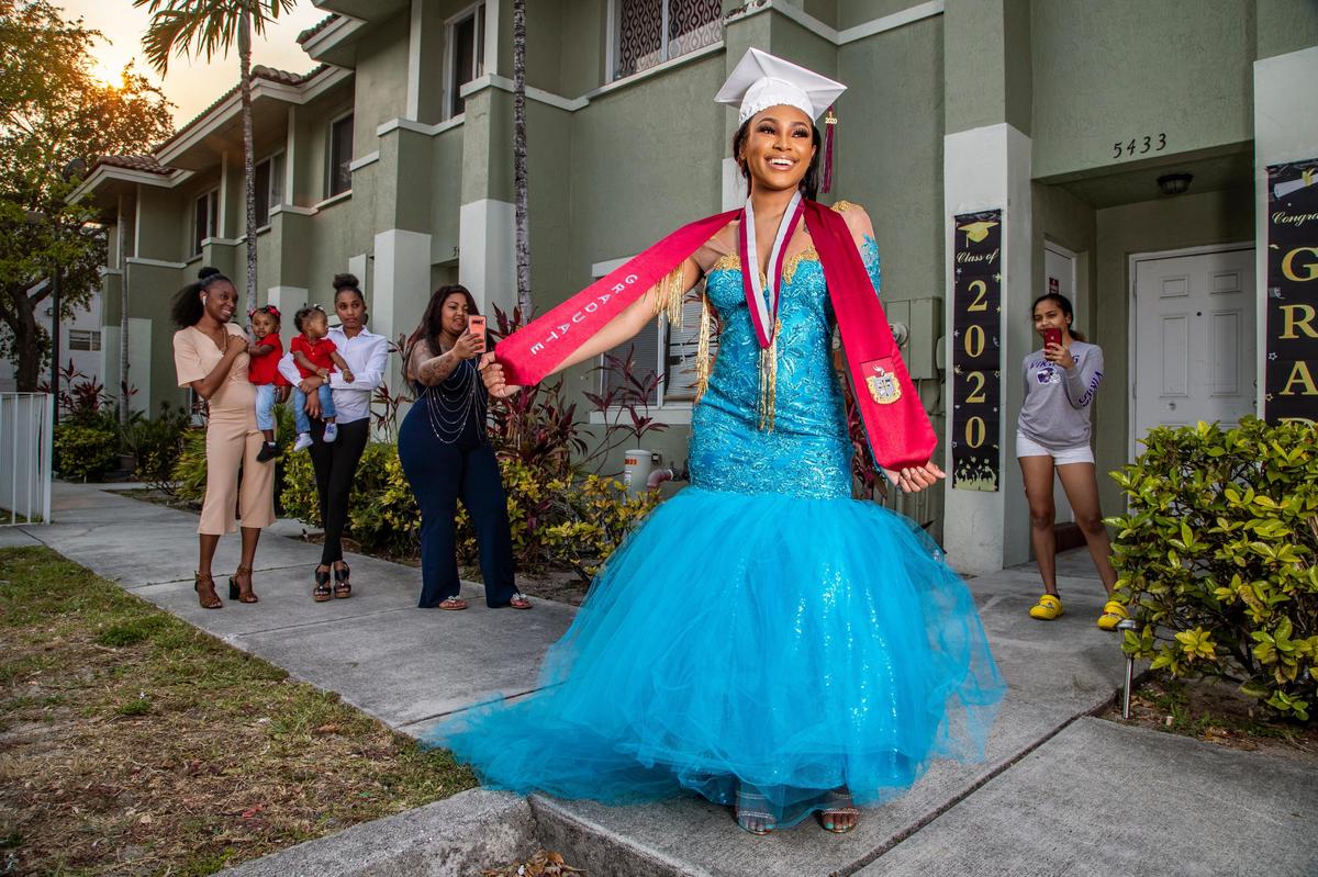 Trenisha Maxwell, 17, of Miami Norland Senior High School, wears her senior prom dress and the graduation cap and sash she would have worn for graduation with her fellow classmates, but the events were canceled due to COVID-19. Her sisters Taquisha Maxwell, holding Summer McCarthy, 1, and Telesha Maxwell, holding Autumn McCarthy, 10 months, are in the background, while her mother, Michelle Maxwell, 41, takes pictures. At right is friend Trinity Wood, 17, who is social distancing.