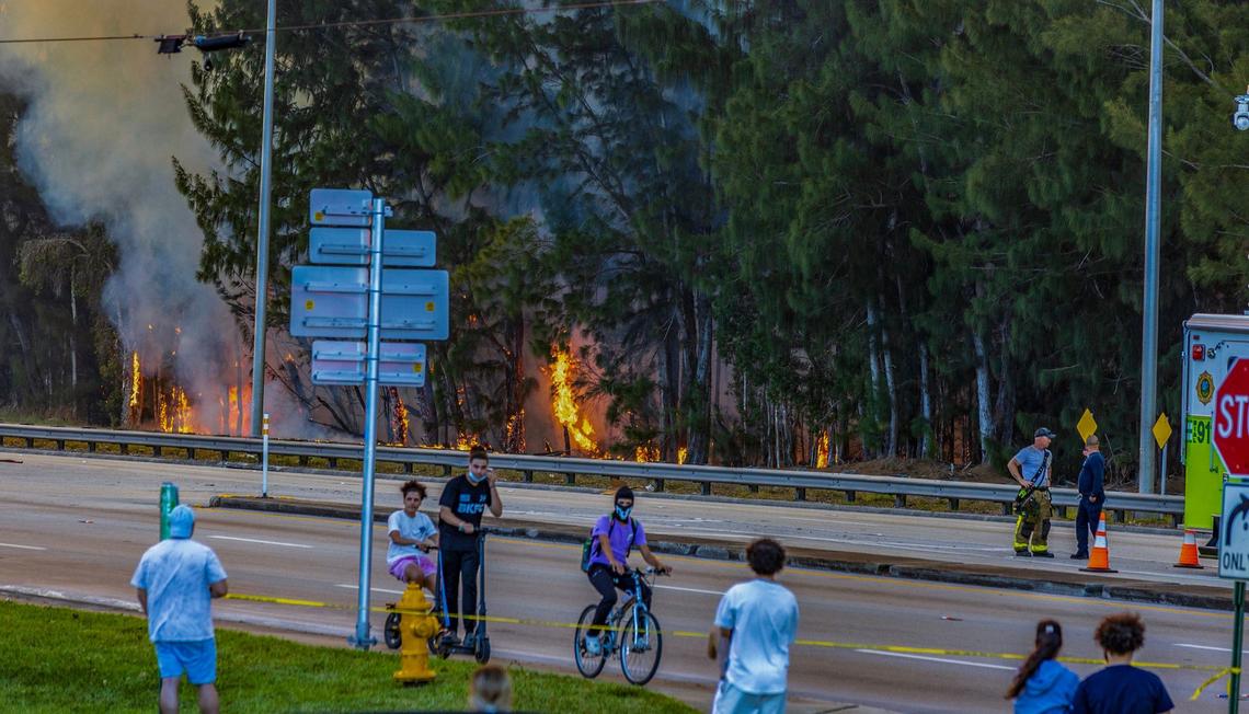 A group of people seen in the sidewalk as police shut down SW 8th Street in both directions due to the heavy smoke caused by a grass fire at SW 137 Avenue and 8 Street in Miami, on Sunday, April 14, 2024.
