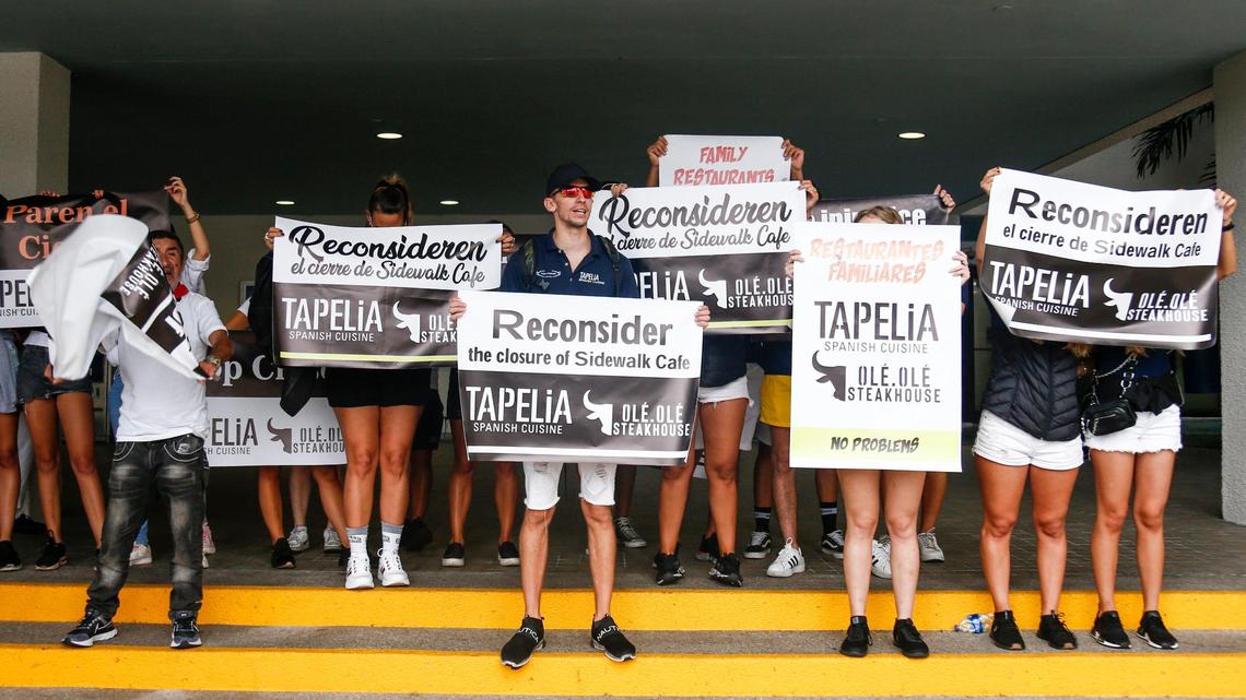 Manifestantes corean y sostienen pancartas durante una protesta frente al Ayuntamiento de Miami Beach el lunes 22 de noviembre de 2021, después que la ciudad negara la renovación de los permisos para comer al aire libre a algunos restaurantes de Miami Beach.