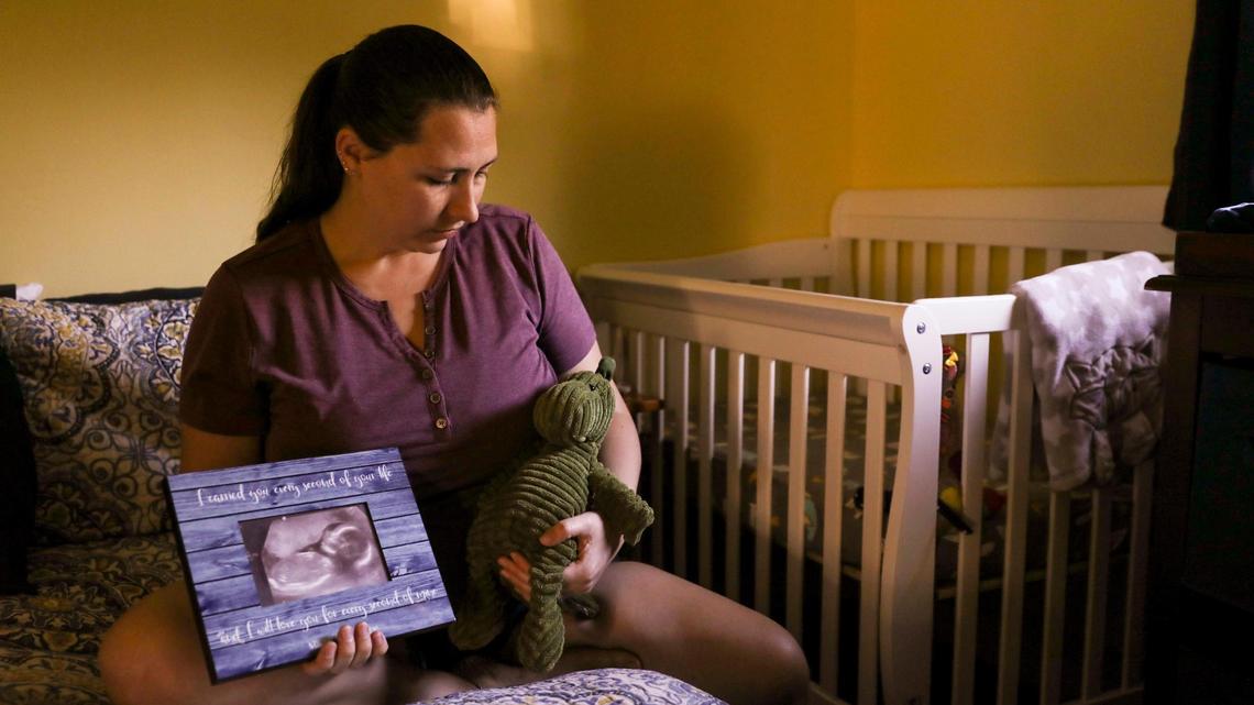 Danielle Tallafuss, 35, poses for a portrait with a sonogram of her son Nathaniel and a corduroy dinosaur she bought for him in her bedroom on Monday, Feb. 21, 2022. Danielle and her husband decided to terminate her pregnancy at 22 weeks after learning that Nathaniel would have been born with hypoplastic left heart syndrome, an underdevelopment of the left side of the heart, to protect their child from the toll his condition would take on his life. “I carried you every second of your life and I will love you for every second of mine,” reads the frame. Danielle said she held onto the dinosaur when she had the abortion.