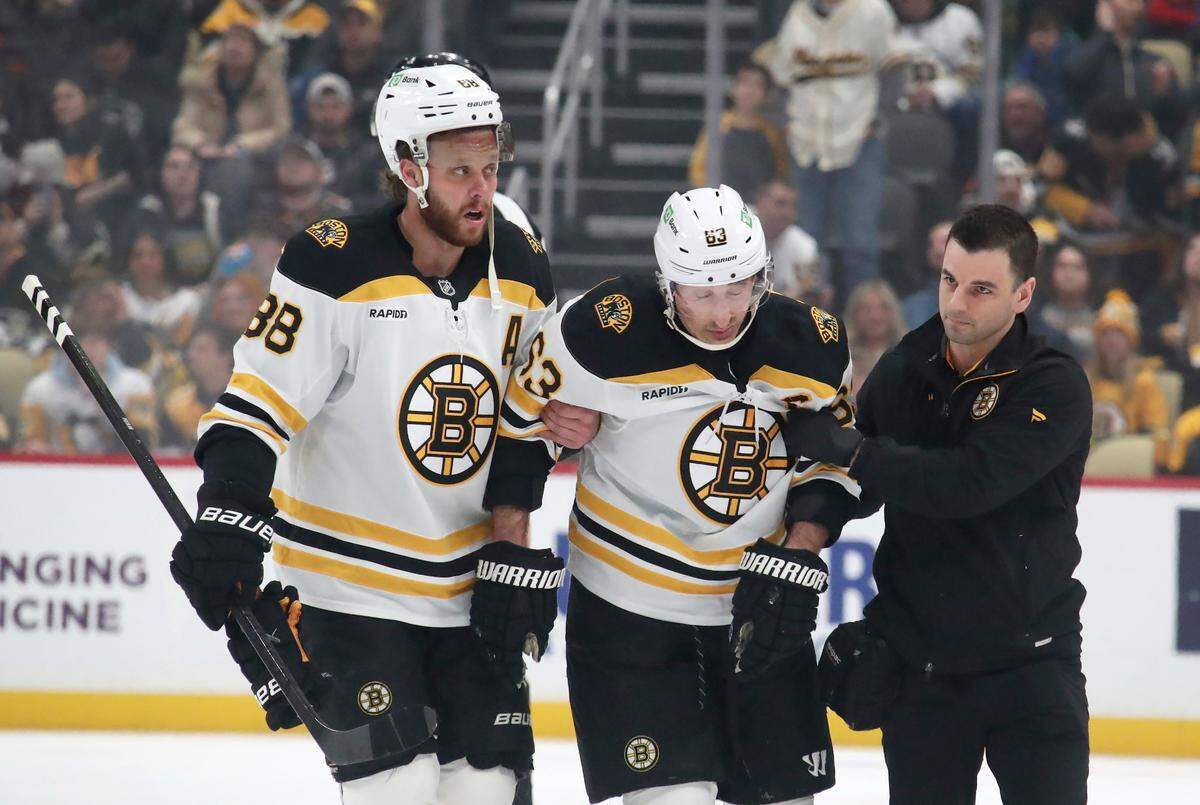 Mar 1, 2025; Pittsburgh, Pennsylvania, USA;  Boston Bruins left wing Brad Marchand (63) is helped from the ice by right wing David Pastrnak (88) and a team trainer after suffering an apparent injury against the Pittsburgh Penguins during the first period at PPG Paints Arena.