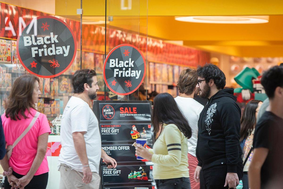 Black Friday shoppers walk by signs advertising deals at Dadeland Mall in Kendall on Friday, Nov. 29, 2024.