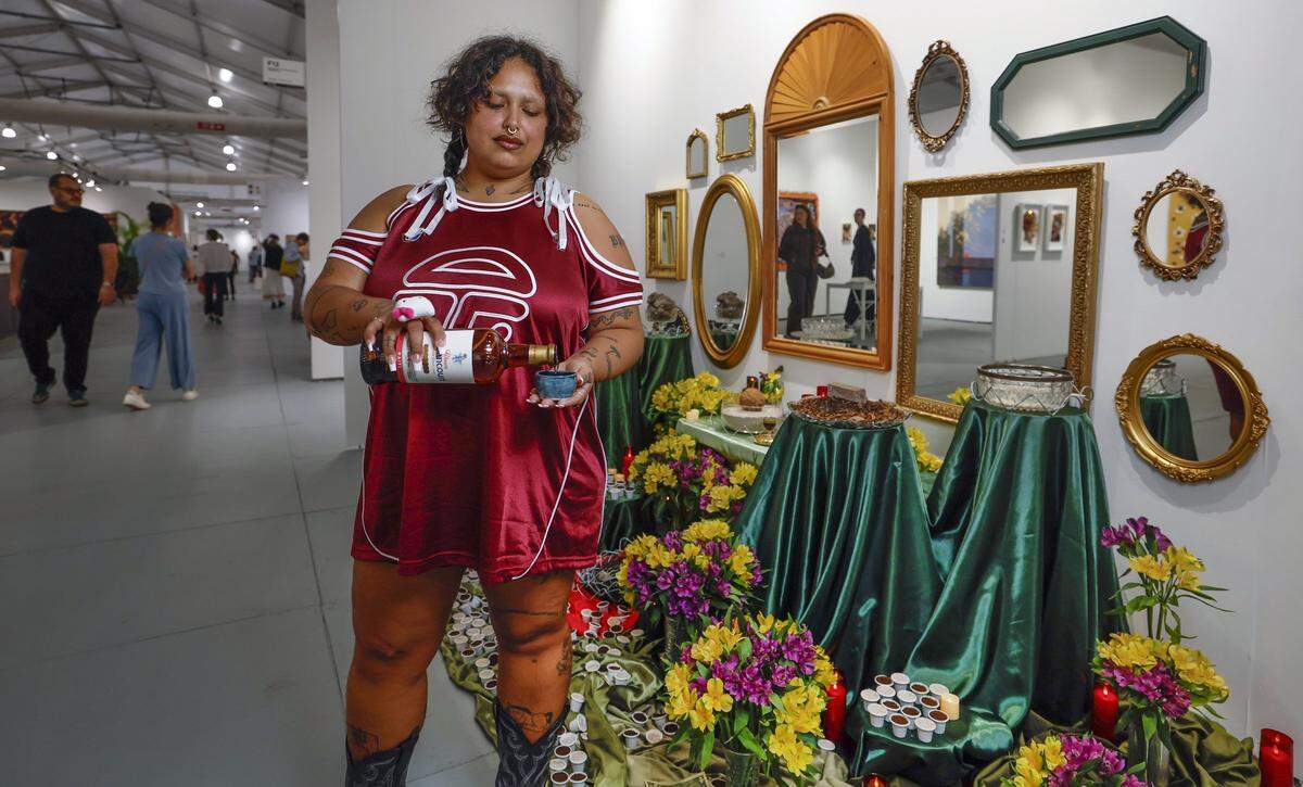 Artist Agua Dolce debuts an installation Untitled (a hope is but a dream is but a plan yet put to action) at this week's SCOPE Art Show protesting the Alligator Alcatraz immigration detention center in the Florida Everglades. Dolce pours a cup of rum as an offering at the alter built in honor of those imprisoned at Alligator Alcatraz is set amid the fair's international art displays at the SCOPE Pavilion on Miami Beach, Florida, on Wednesday, December 3, 2025. 