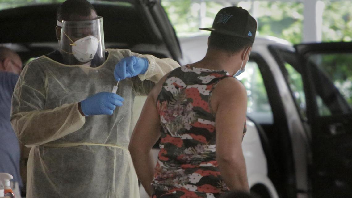 A man who just got tested for COVID-19 walks away, right, as the EMT worker who administered the test safely deposits the nasal swab into its container at the Caleb Center Garage in Miami.