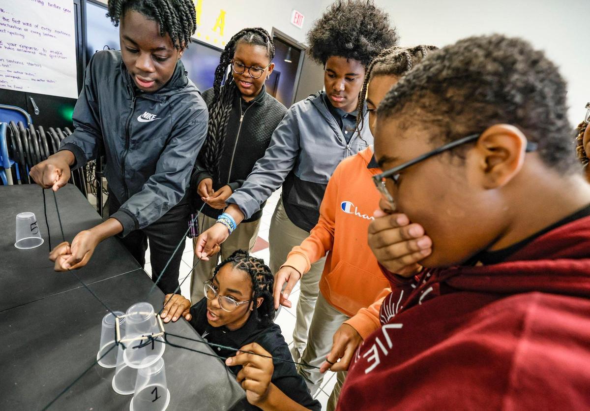 Payton Rigby, 12, Emma Hunter, 12, Khristian Benn, 13, Jarvis Benn,11, Zahri Kitchen, 12, standing left to right, and Journey White, 13, at bottom, collaborate as they play the cup challenge at Urgent Academy Middle School.