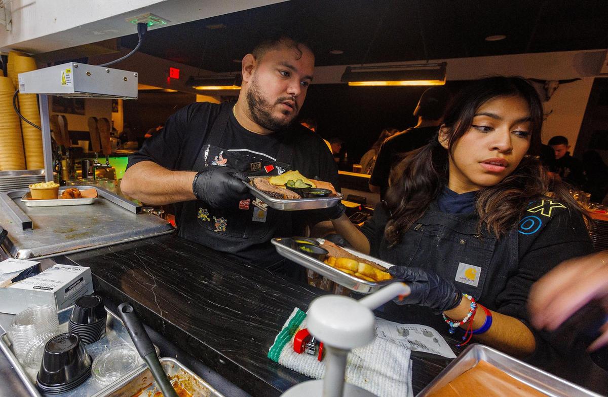 Servers Leslie Bustos and Ruben Ojeda rush to serve orders from the kitchen of Apocalypse BBQ.