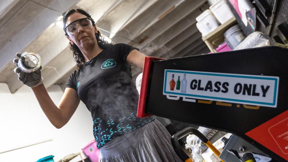 La cofundadora de Glass For Life, Paola Barranco, empujando una botella de vidrio a través de un pulverizador para crear arena en el almacén de la empresa, el martes 28 de mayo de 2024 en Miami.