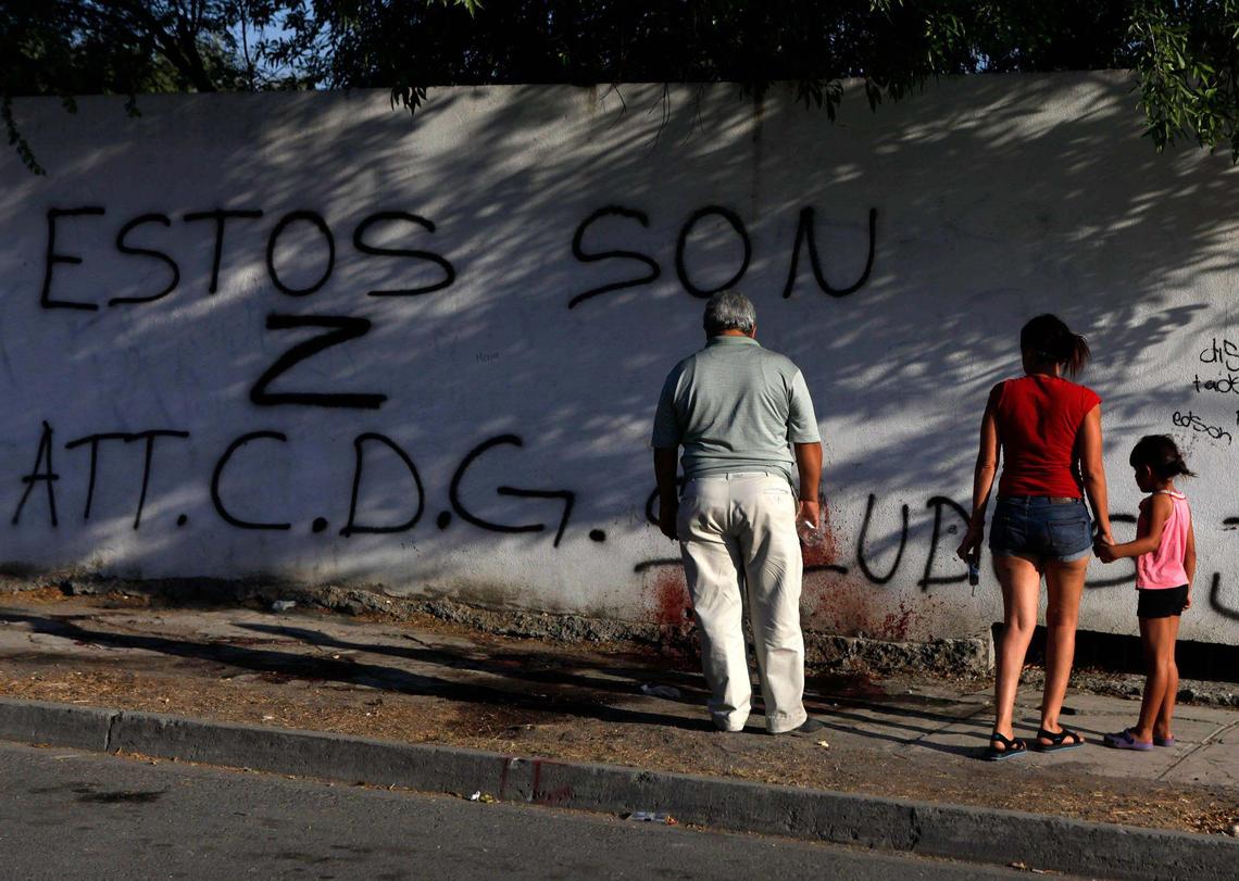 Residents examine blood stains and graffiti left by gunmen at a crime scene in Monterrey, Mexico, June 15, 2011. Hitmen killed three men at the scene and tried to set them on fire.