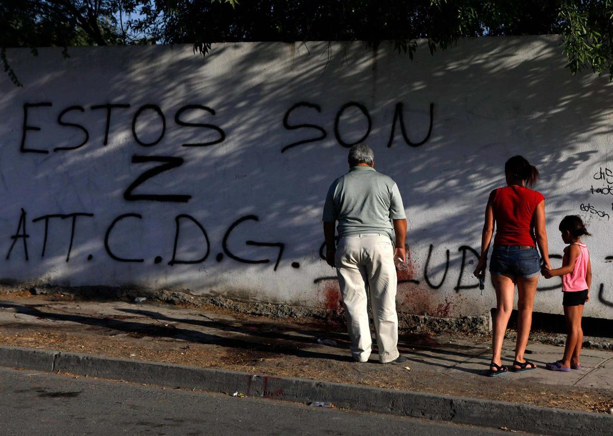 Residents examine blood stains and graffiti left by gunmen at a crime scene in Monterrey, Mexico, June 15, 2011. Hitmen killed three men at the scene and tried to set them on fire.