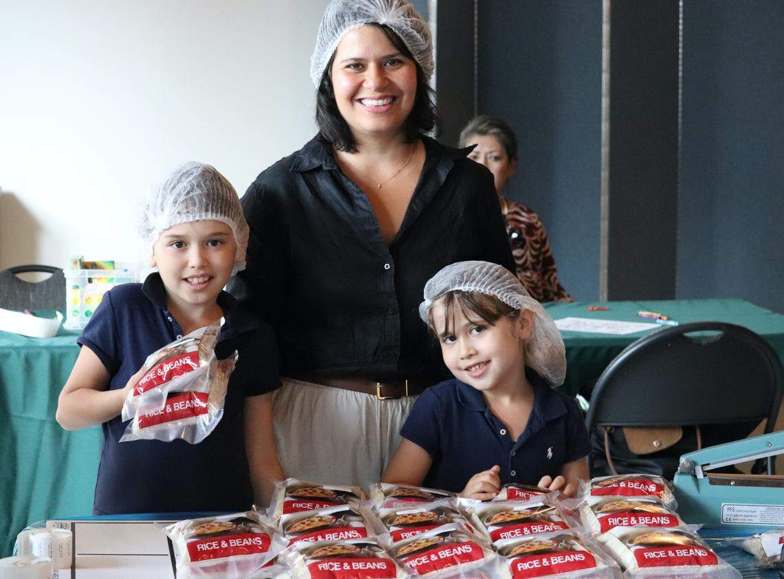 Juliana Warsaw and her daughters Grace, 8, and Gabrielle, 5, work together to put packages of rice and beans into boxes during a food packing event at St. Augustine church in Coral Gables on Friday, April 1, 2022.