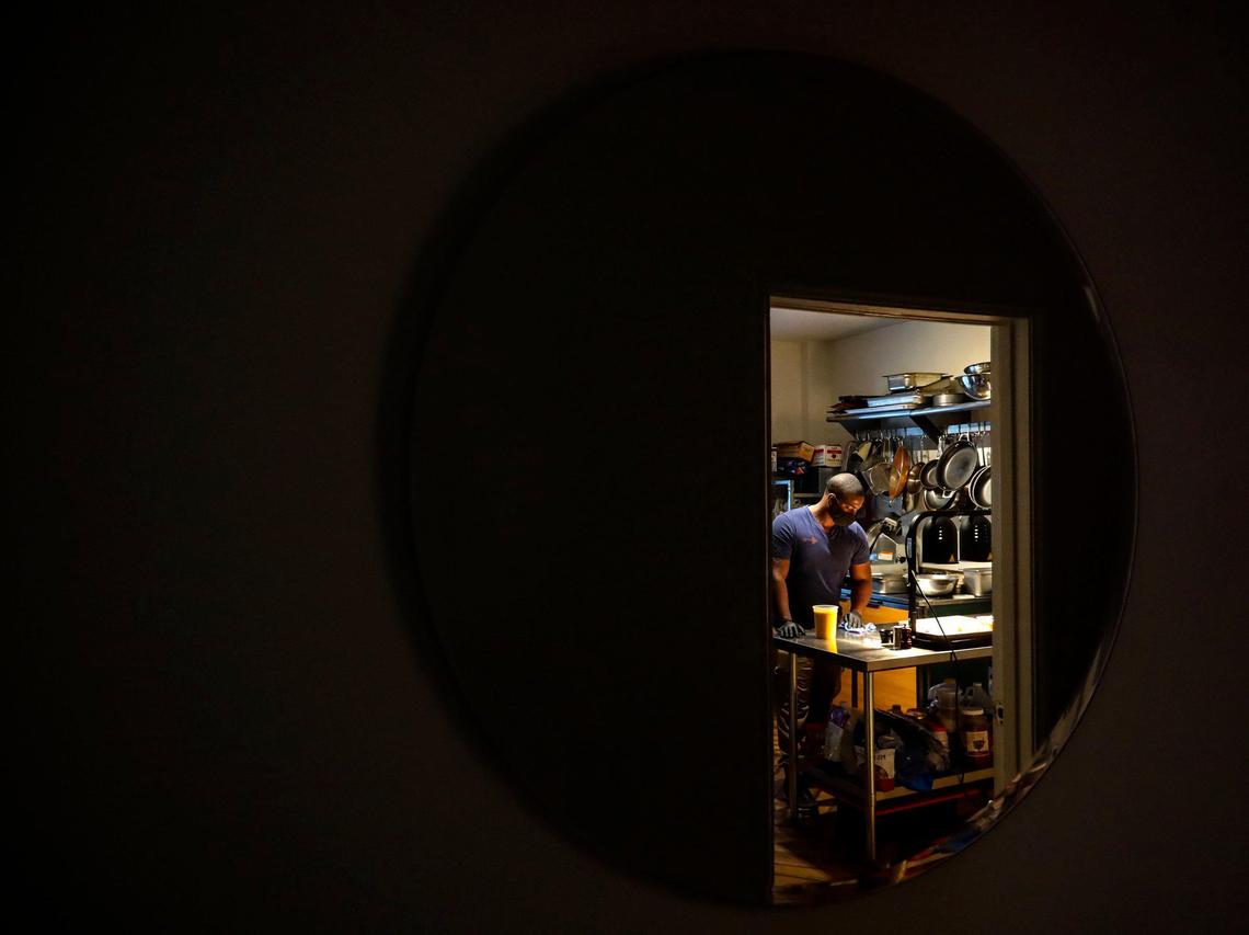 The hallway mirror in their darkened, closed Copper Door Bed & Breakfast captures Akino West cleaning the counter as he helps with fying chicken and waffles for volunteers.