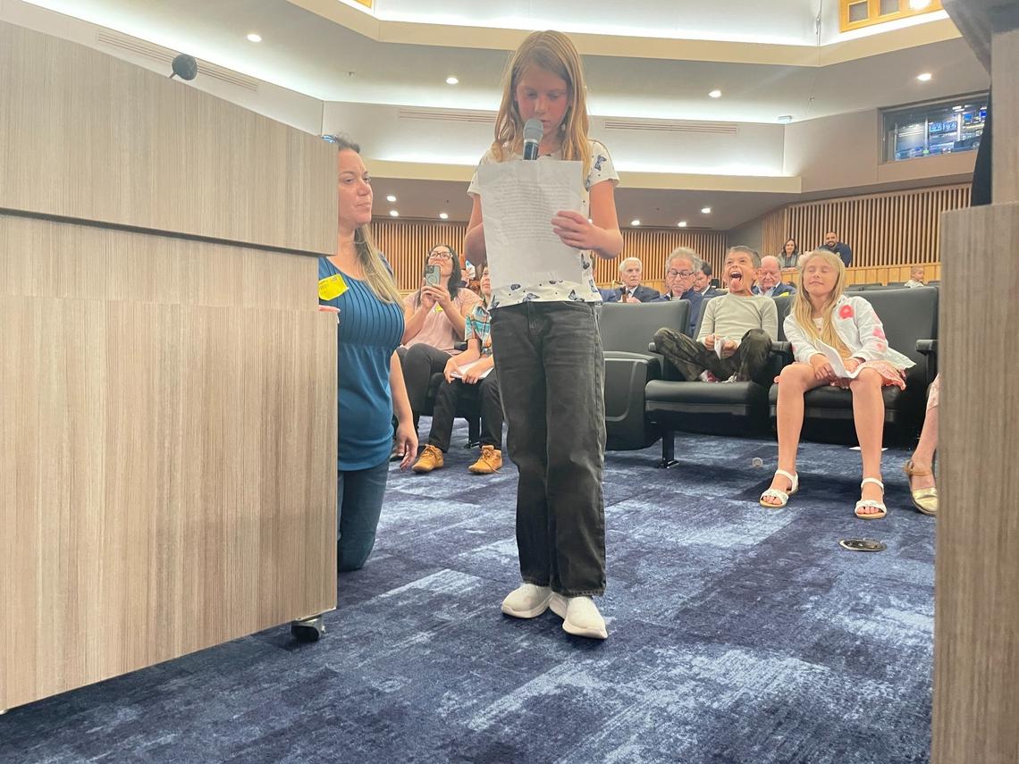 Lilly Pfaff, 8, of Davie, reads remarks urging Miami-Dade County commissioners to remove fluoride from drinking water as her mother, Cynthia Pfaff, kneels beside her at the lectern.