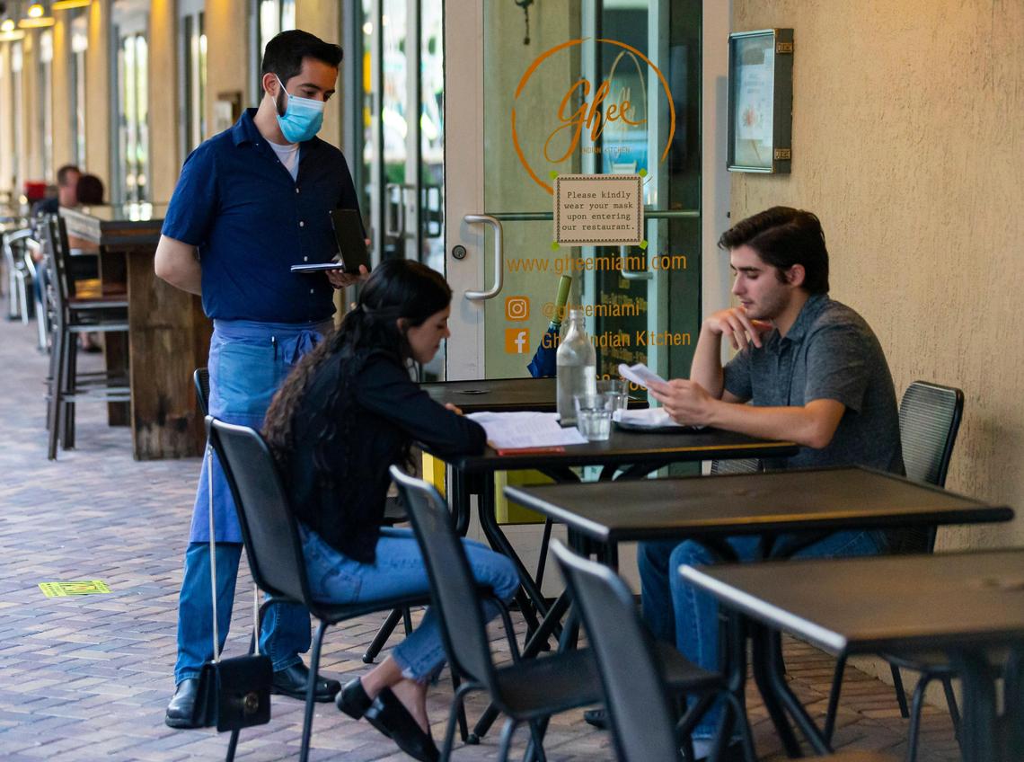 Alonso Escalante, 33, a waiter at Ghee Indian Kitchen, takes down an order from guests visiting the restaurant in Dadeland on Wednesday, May 20, 2020. Escalante was anxious about returning to a job where he deals with the public all day but said he feels safe with the procedures in place..