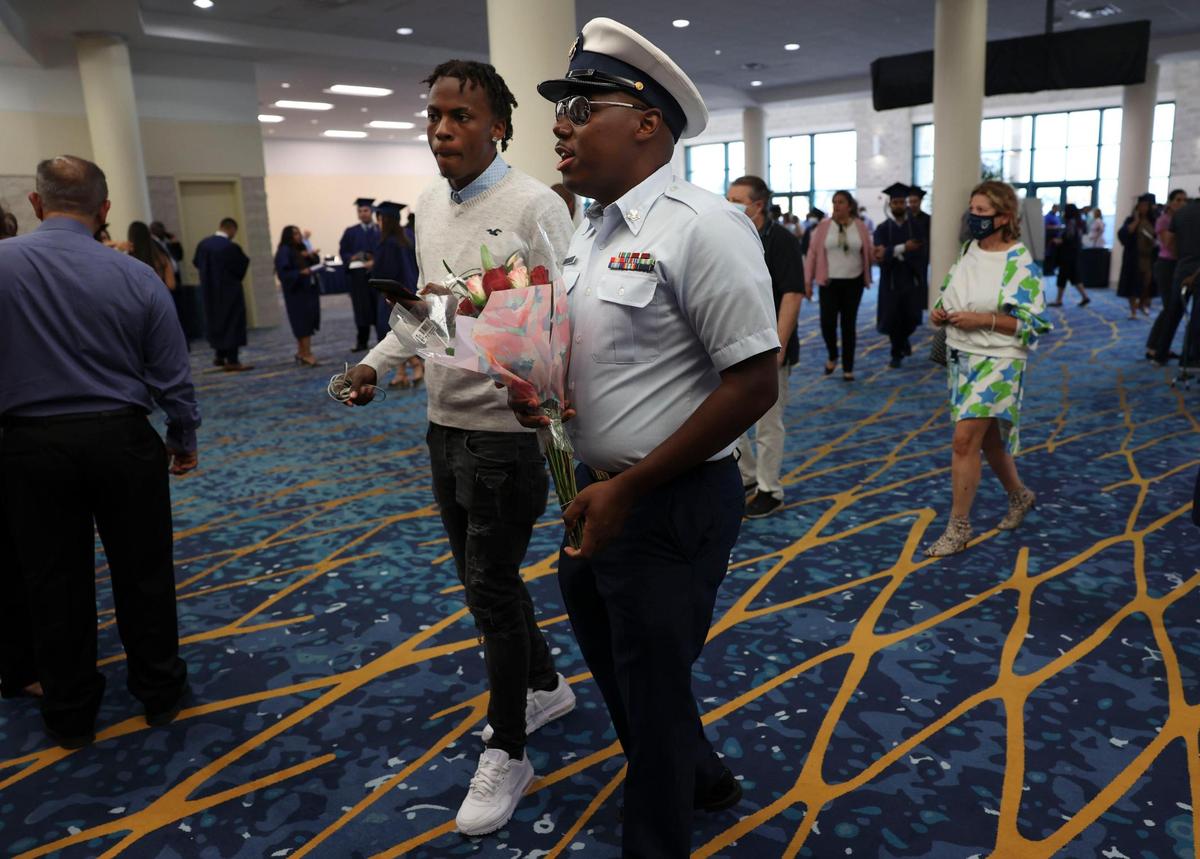 Marcus Roberts, U.S. Coast Guardsman, right, along with his cousin, Trovex Bain, prepares to surprise his mother, Jennifer Freeman, 54, before her graduation from Broward College at the Broward County Convention Center in Fort Lauderdale on Thursday, May 5, 2022. Roberts was stationed in Malta and was not going to be able to attend her graduation. When he found out his deployment was shortened, he surprised her.