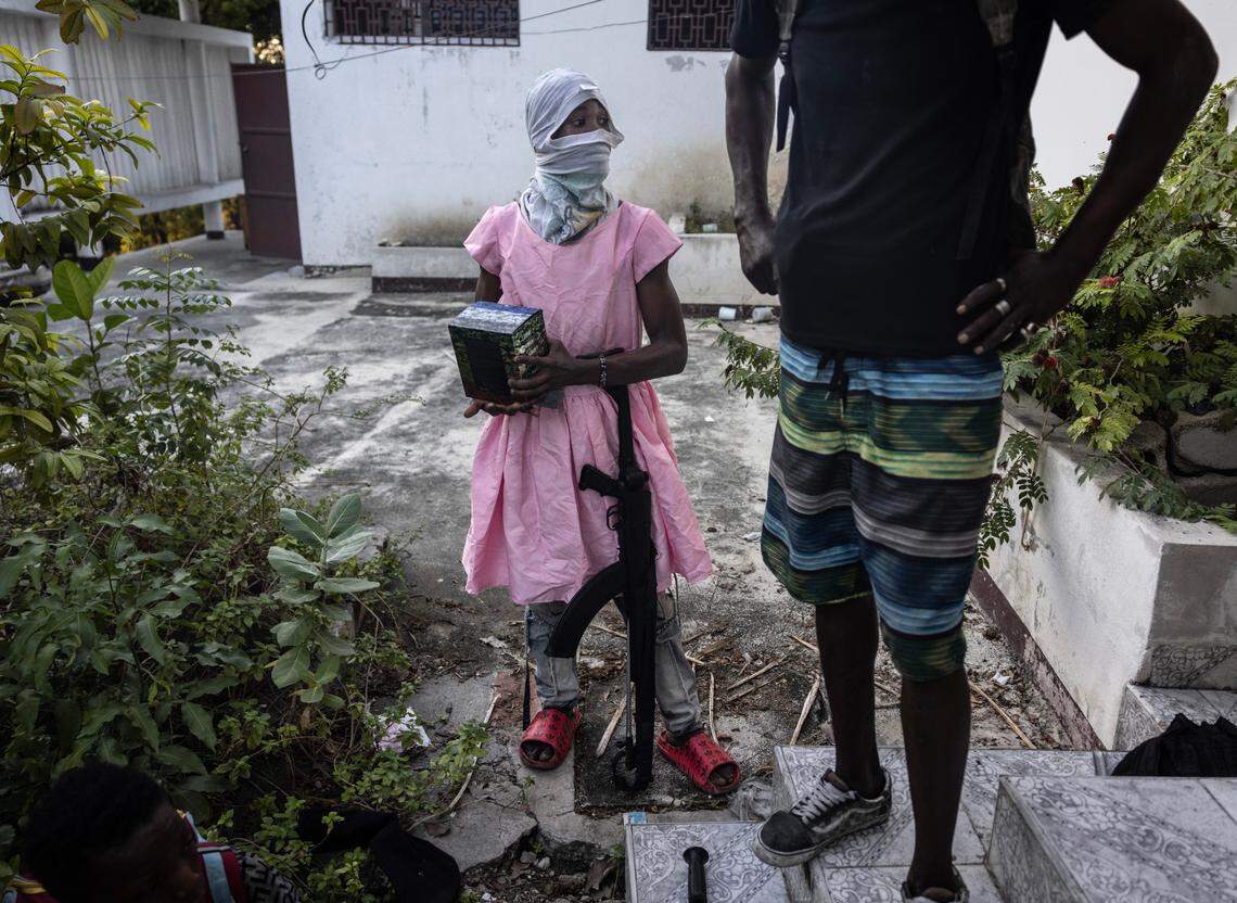 A teenage gang member wears a dress and stands with an AK-47 rifle after he raided a neighborhood of Port-au-Prince with other gang members, on Dec. 6, 2024. The boy stole the dress during the raid and thought that wearing it would be easier than carrying it.