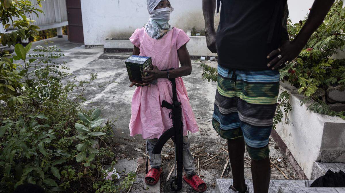 A teenager stands with an AK-47 rifle after he raided a neighbourhood of Port-au-Prince with other gang members on Dec. 6, 2024. The boy stole the dress during the raid and thought that wearing it would be easier than carrying it.