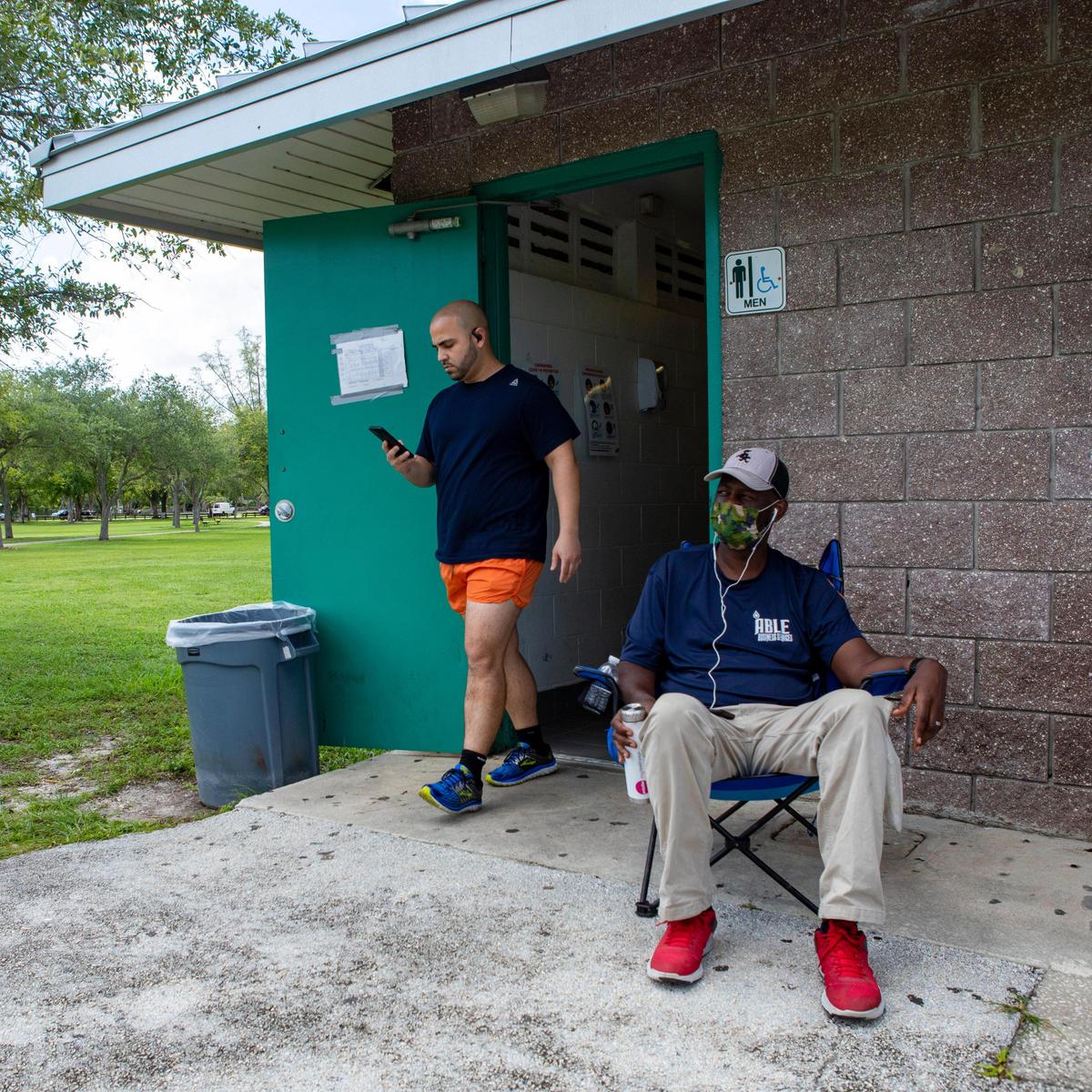 A visitor to Tropical Park exits the men’s public bathroom as Derek Kearney, an Able Business Services employee, sits at his post in between cleaning the restrooms on Friday.