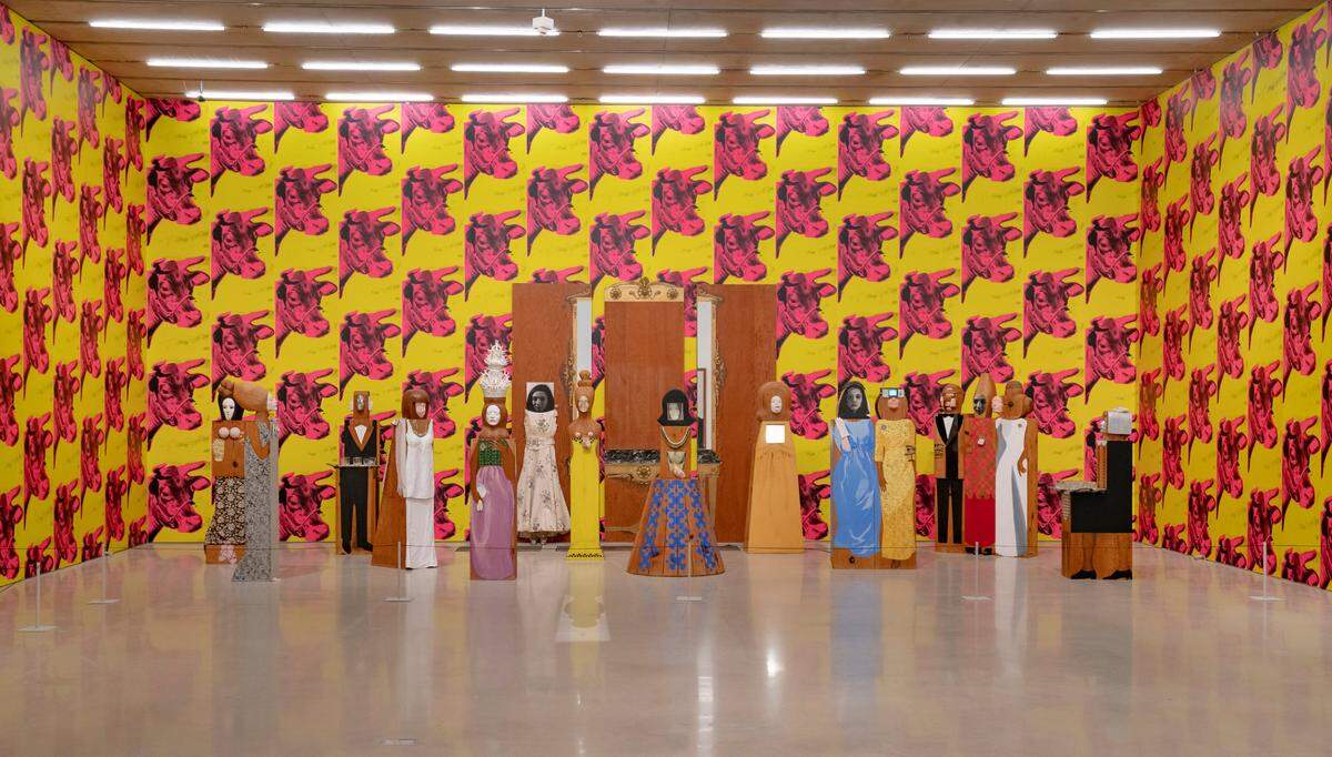 The final section of the exhibition features two works by Andy Warhol and Marisol that were originally debuted as installations in New York City galleries in 1966. The walls are plastered in Warhol’s hot pink and yellow cow wallpaper. On the ground is “The Party,” a group of over a dozen nicely dressed party guests that all share Marisol’s face.