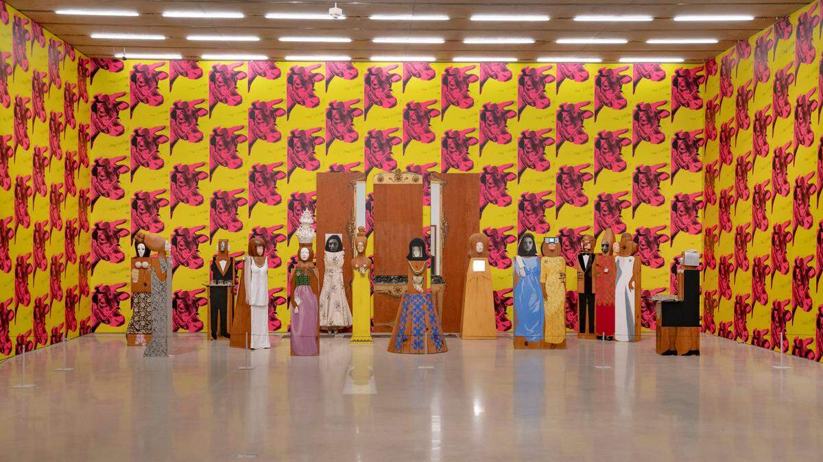 The final section of the exhibition features two works by Andy Warhol and Marisol that were originally debuted as installations in New York City galleries in 1966. The walls are plastered in Warhol’s hot pink and yellow cow wallpaper. On the ground is “The Party,” a group of over a dozen nicely dressed party guests that all share Marisol’s face.
