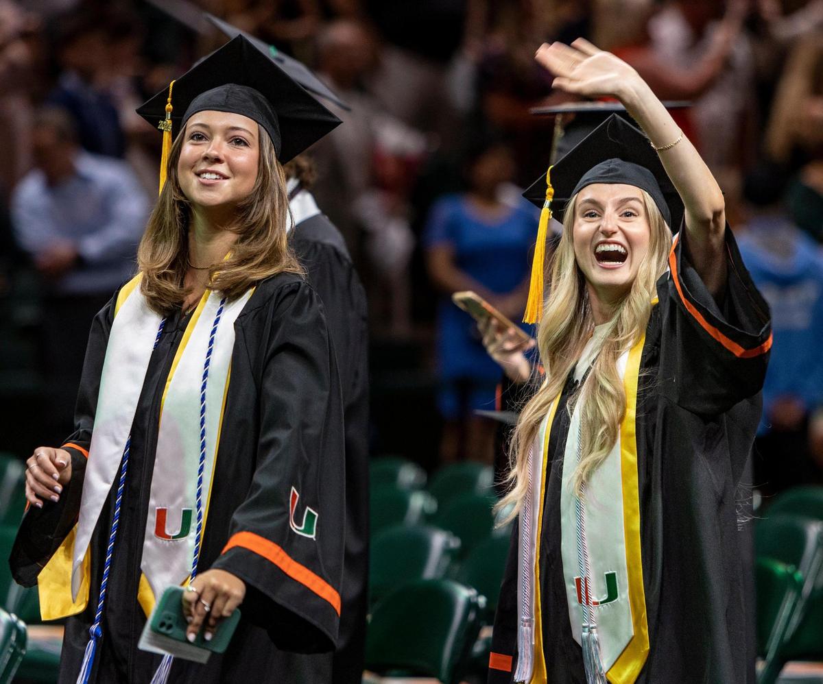 Gillian Drexler, right, greets her family in the stands as Charleigh Peters, left, leads the way down the aisle as they enter the Watsco Cente for UM’s spring commencement ceremonies Friday morning. Drexler majored in biochemistry and molecular biology and art, and minored in chemistry, and wants to become a dentist next.