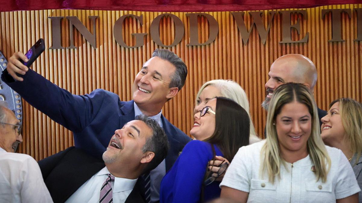 Miami-Dade commissioner, René Garcia, left, tries for a selfie with Jacqueline García-Roves, center, after she was sworn in as interim mayor of Hialeah, marking a historic milestone as she became the first woman to assume this position in the 100-year history of the city on Monday, April 28, 2025, in Hialeah’s City Hall.