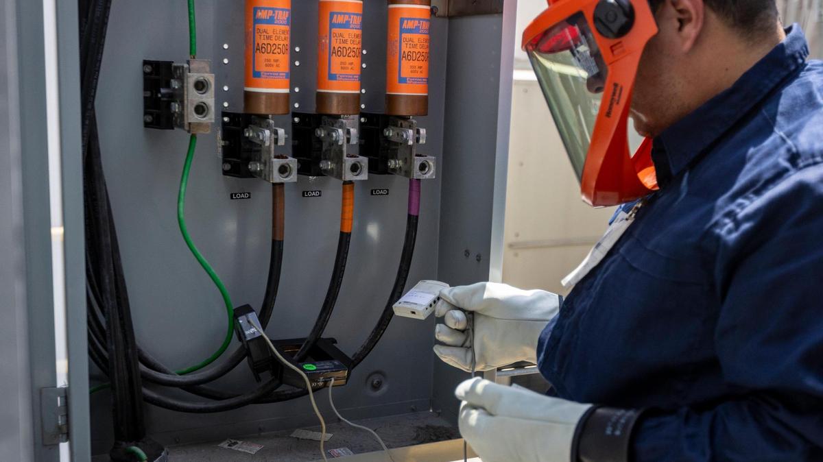 Wearing an electricity-resistant Arc Flash suit, Dr. Ibrahim Ahmed attaches sensors to power lines to collect data on the energy use of two large air conditioning units. Auditors from the University of Miami Industrial Assessment Center measured the energy and water efficiency of an office building in Coral Gables on Sept. 1.