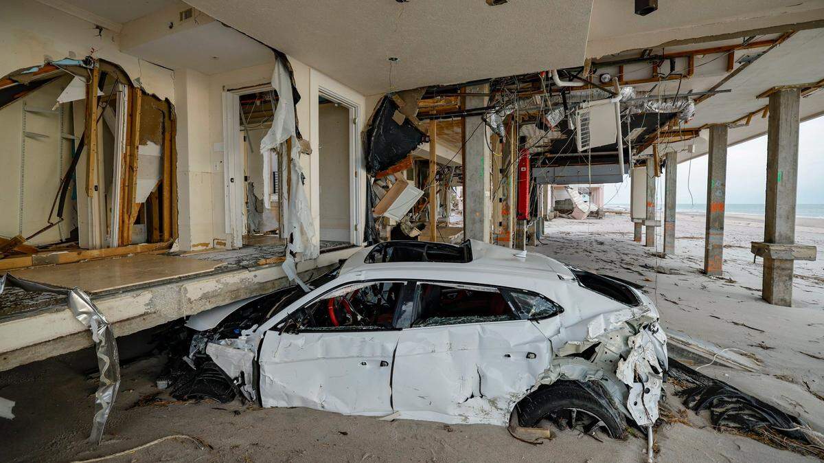 A damaged Lamborghini sits under a house two days after several feet of beach sand washed ashore from hurricanes Helene and Milton.