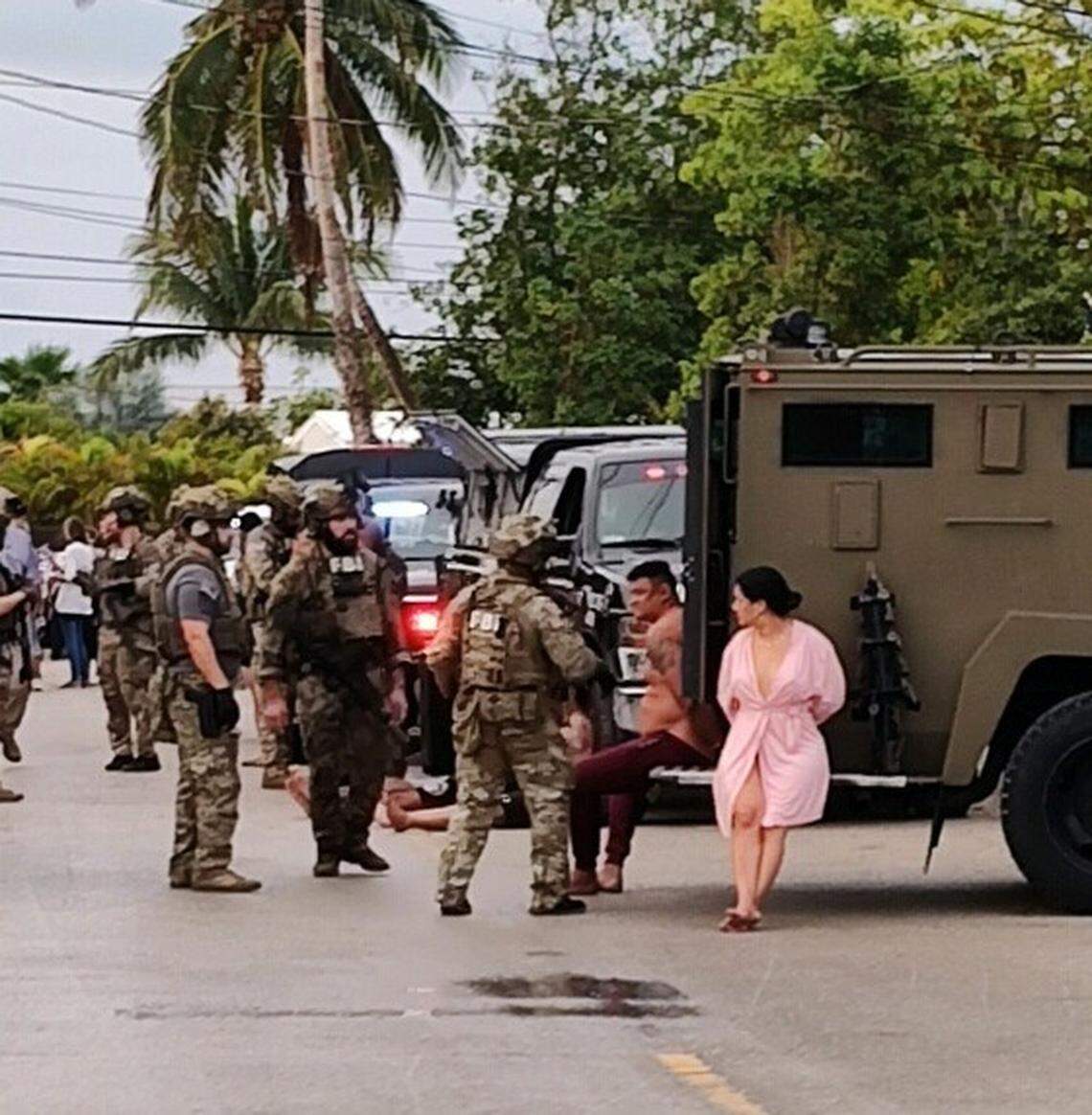 Several people sit and stand handcuffed following a raid by FBI agents on a Geiger Key home Friday, Dec. 16, 2022.