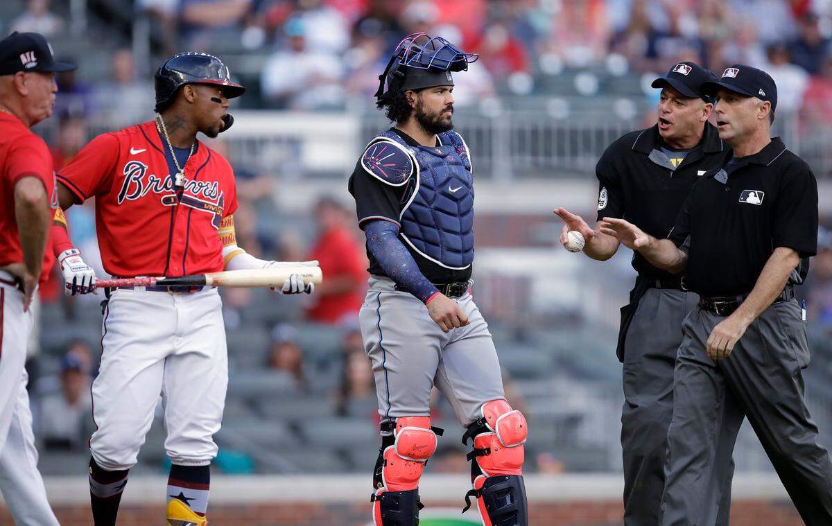Umpires speak with Atlanta Braves’ Ronald Acuna Jr., holding bat, and manager Brian Snitker, left, as Miami Marlins catcher Jorge Alfaro, center, looks on after Acuna was hit by the first pitch thrown by Marlins’ Pablo Lopez in the first inning of a baseball game Friday, July 2, 2021, in Atlanta. (AP Photo/Ben Margot)