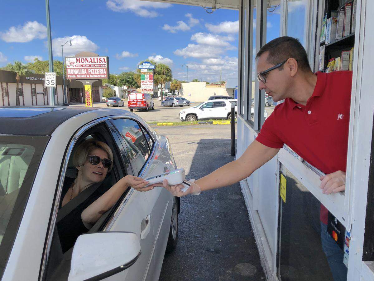 Pedro Hernández, gerente del Farm Stores en 4741 SW Calle Ocho, entrega artículos por la ventana con los guantes puestos. Hernández pidió a la cliente, Vanessa Armas, que ella misma deslizara la tarjeta para pagar.