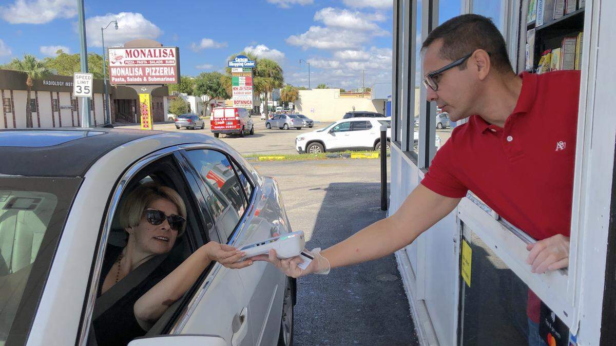 Pedro Hernandez, general manager of the Farm Stores at 4741 SW Eighth Street, dispenses groceries through a window while wearing gloves. He asked customer Vanessa Armas to swipe her own card.