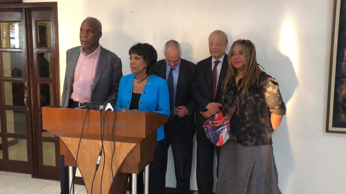 U.S. Rep. Maxine Waters, in blue, speaks to the media in Haiti after an impromptu visit to the country on Wednesday, April 24. Among those who joined her were actor and activist Danny Glover (far left).