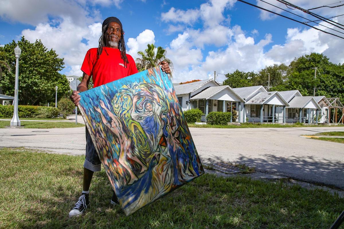 Coconut Grove resident Reinaldo Rose, 69, holds a painting by artist Neith Nevelson who once lived in one of the 1938 historic homes that face Brooker Street, seen at right. The cottages are in Coral Gables, adjacent to the West Grove section of Coconut Grove.