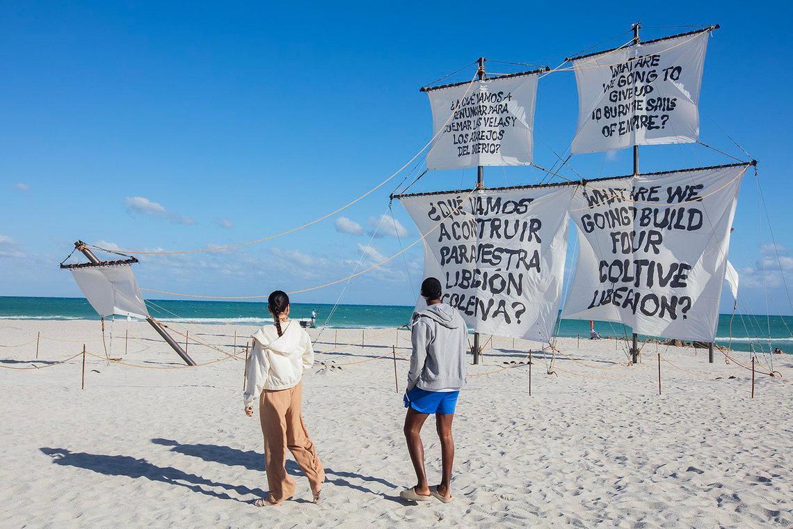 Rode Napoles y Carlos Ramos observan “Seletega”, una escultura de 90 pies de largo de un galeón español naufragado, parcialmente enterrada en la arena por el artista Nicholas Galanin en la arena del Hotel Faena en Miami Beach.