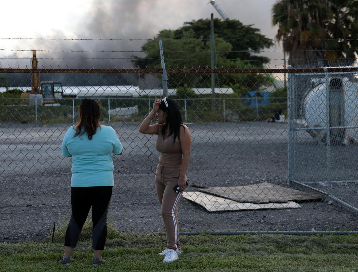 Vendors and shoppers watch as Miami-Dade firefighters battle the fire at a flea market in Miami, Florida on Thursday, July 7, 2022.